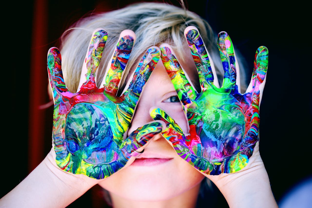 about-us Vibrant close-up of a child's hands covered in colorful paint, expressing creativity and fun.
